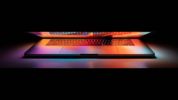 Colorful lights coming from the screen and keyboard of a laptop against a dark background.