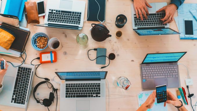 Overhead view of multiple open laptops on a wooden tabletop.