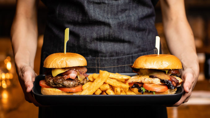 Server holding plate with a cheeseburger and chicken burger along with french fries between the two burgers.