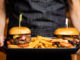 Server holding plate with a cheeseburger and chicken burger along with french fries between the two burgers.