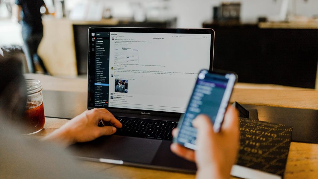 User with open laptop on table and mobile phone in hand.